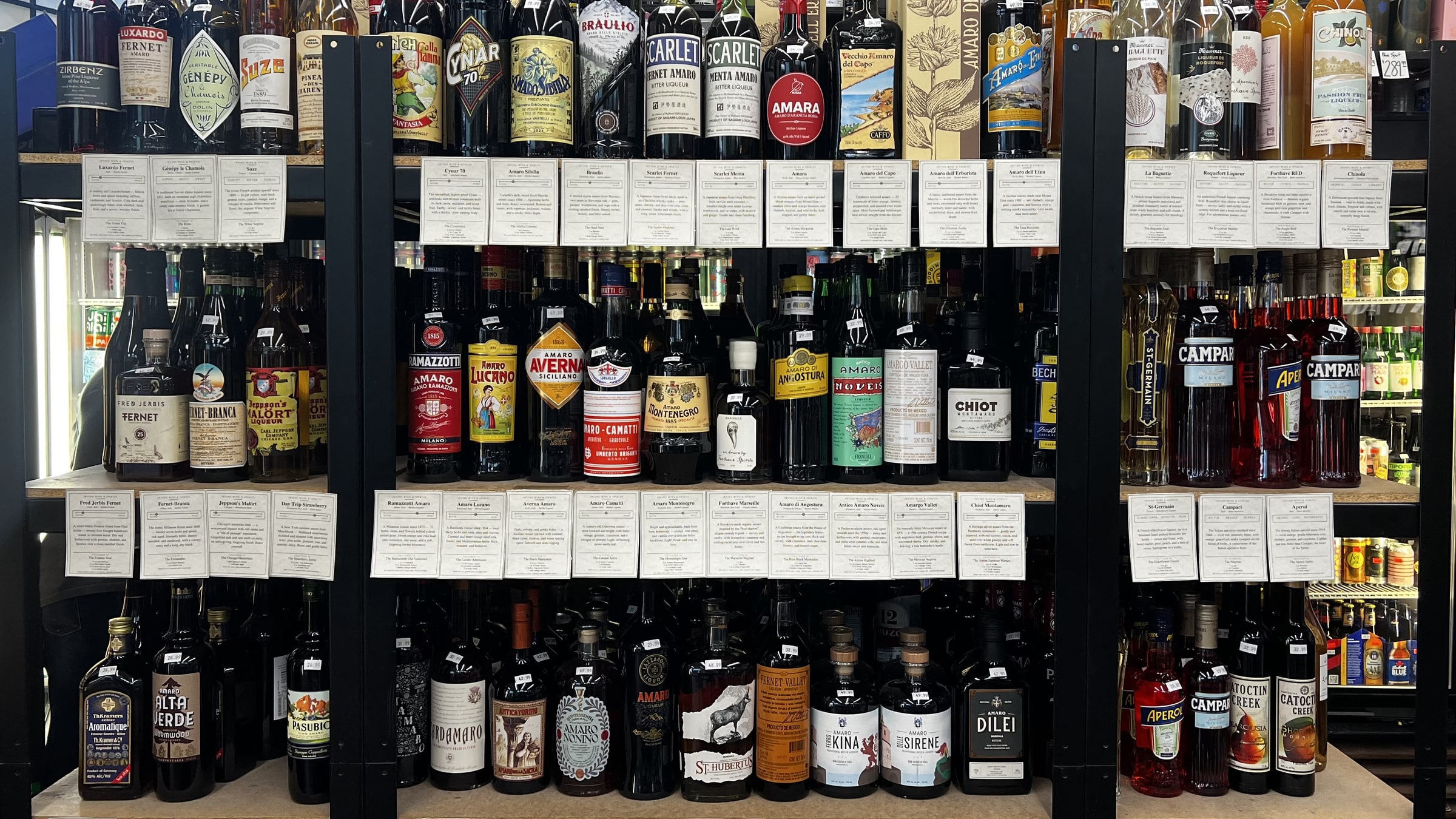 The amaro wall at Irving Wine & Spirits — three shelves deep, every bottle with a hand-written shelf-talker. The visual proof of the curation.