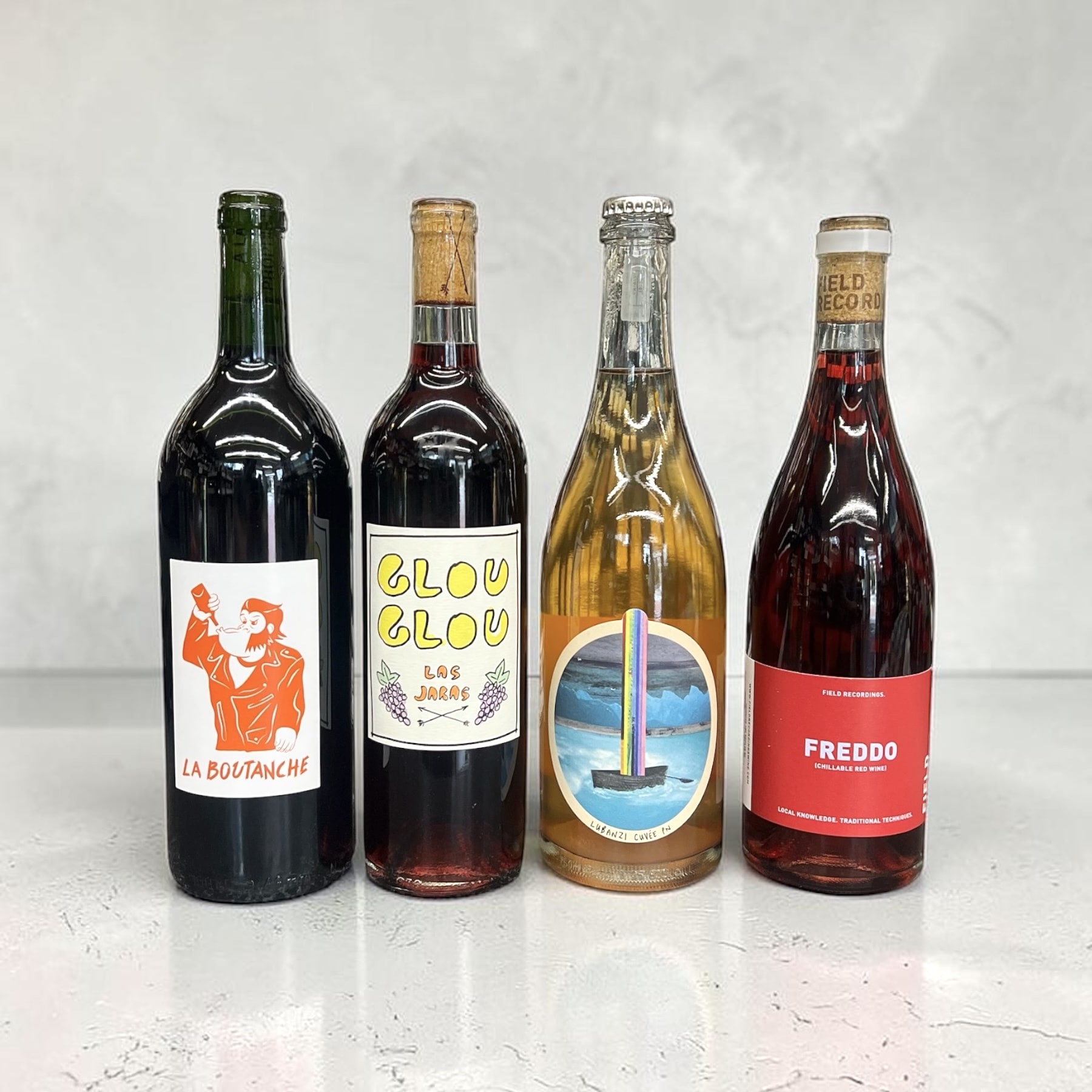 Four natural wine bottles from the Irving Wine & Spirits shelf — La Boutanche red, Las Jaras 'Glou Glou,' the Lubanzi 'Rainboat' pét-nat, and Field Recordings 'Freddo' chillable red — labels you'd want to pick up.