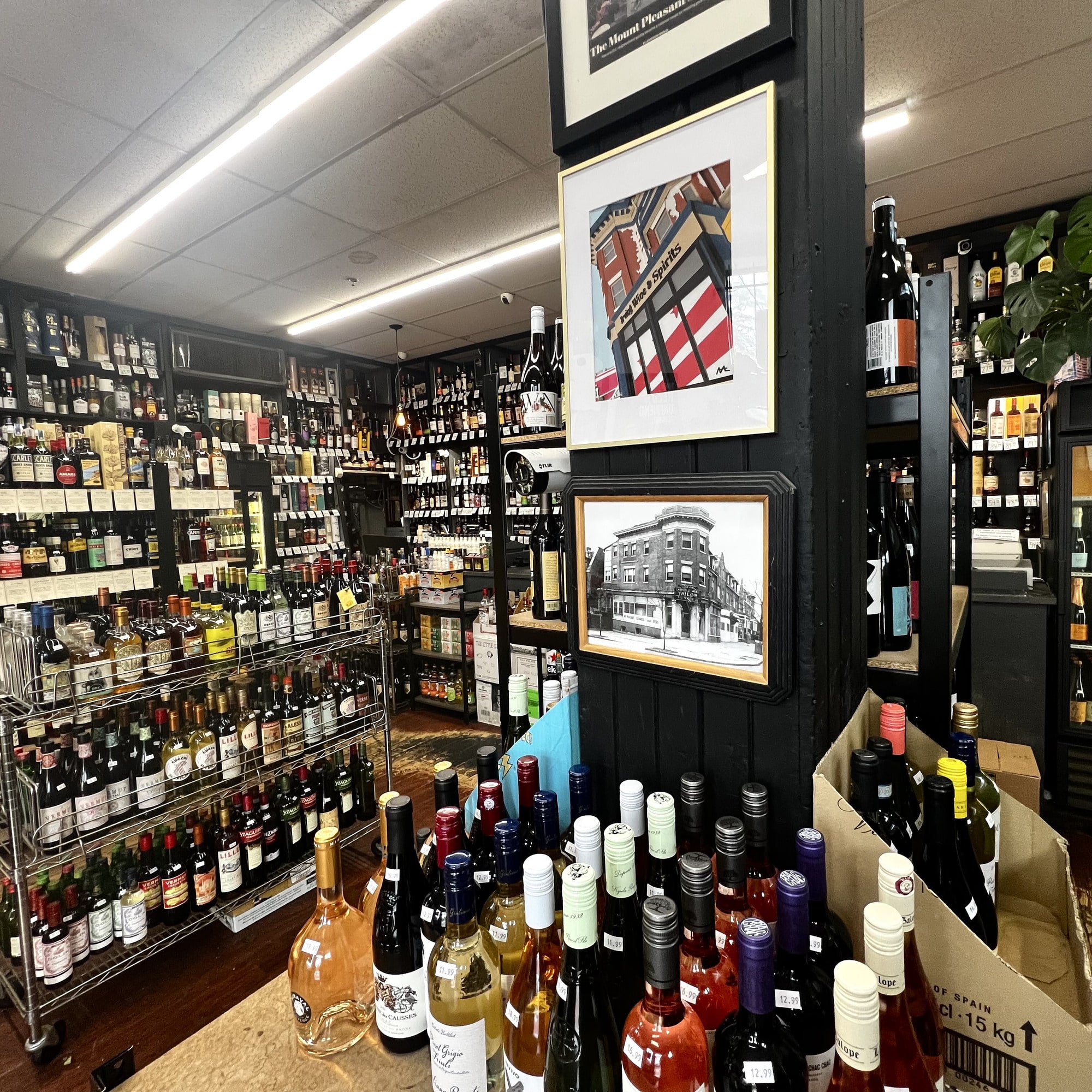 Inside Irving Wine & Spirits today — wine shelves lined floor to ceiling, a rack of bottles down the aisle, and framed historical photos of the corner building mounted on the column.