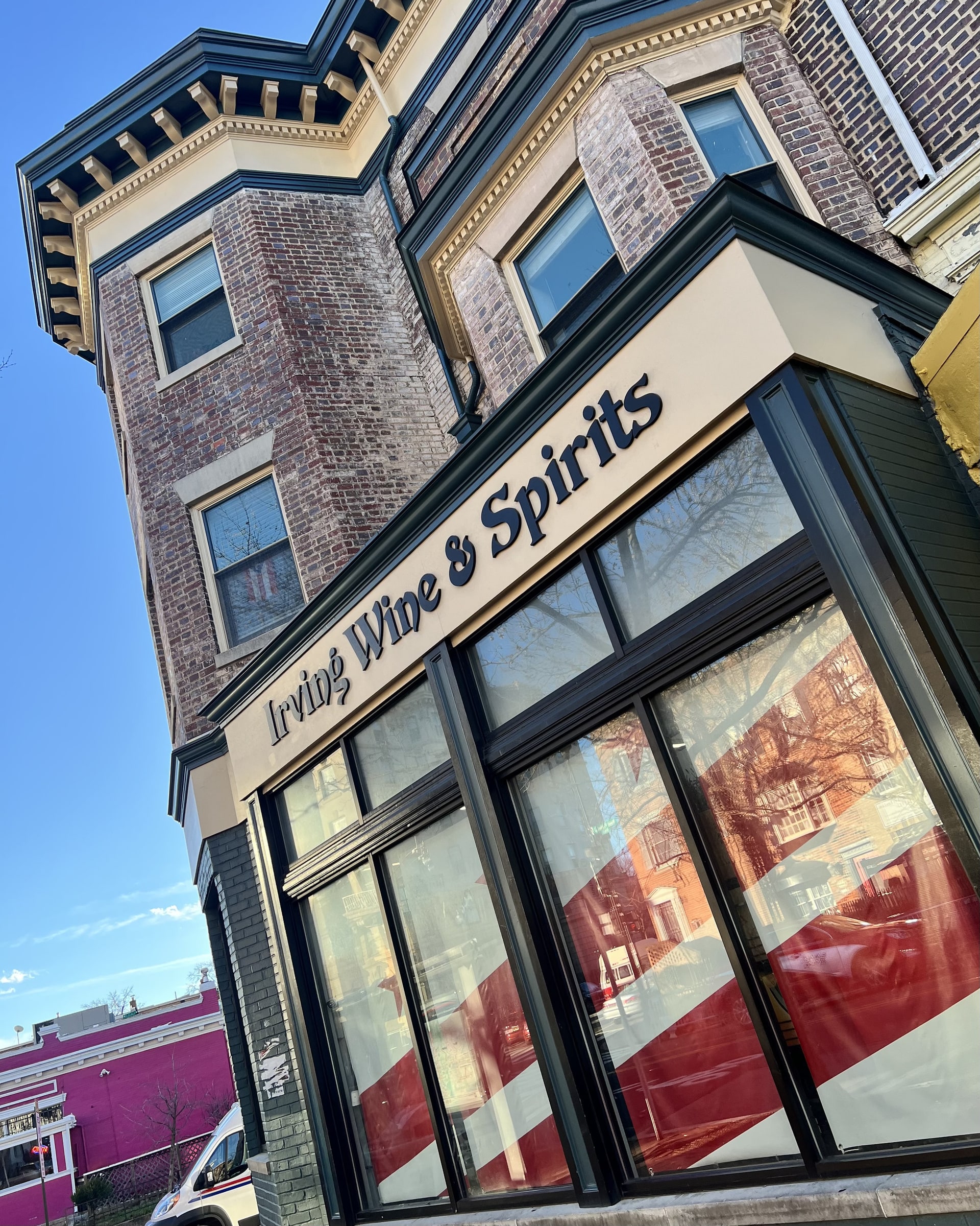The Irving Wine & Spirits storefront on the corner of Mt. Pleasant Street NW — the painted 'Irving Wine & Spirits' window sign on the brick turret building against a blue sky.